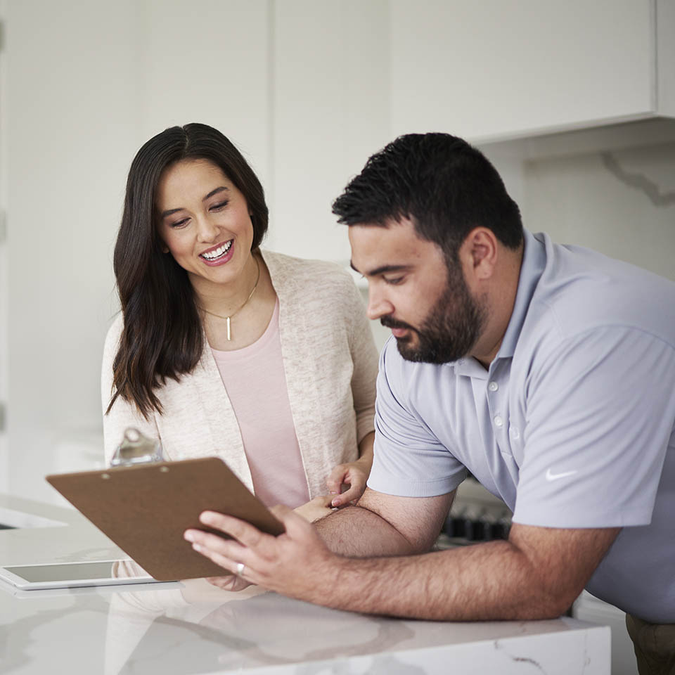 A man and woman in a home, looking at a clipboard together.